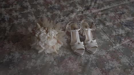 zapatos de novia blancos emparejados con un delicado ramo con rosas blancas y acentos suaves, colocados en una tela con patrones florales