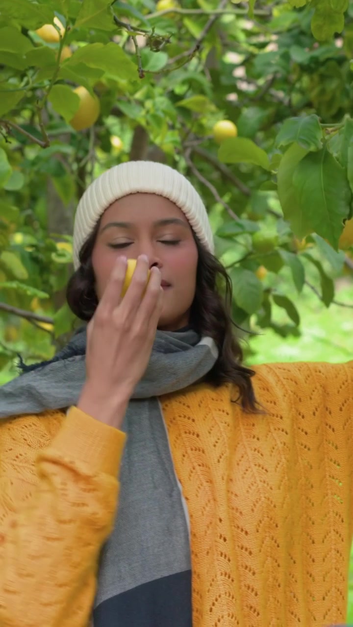Video verticale: Uomo con felpa con cappuccio che entra, donna con maglione giallo che raccoglie frutta da un albero in giardino.