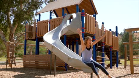 slow motion of woman having fun going down a slide at a park