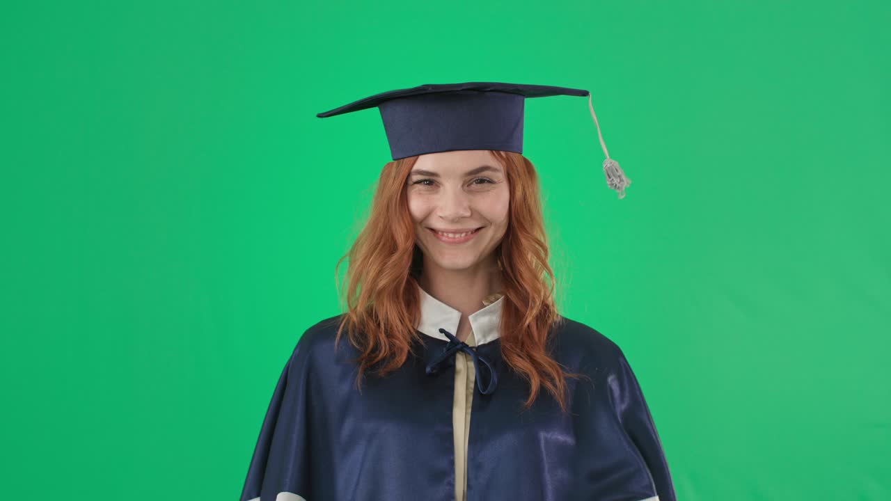 laurea online, ritratto di una ragazza emozionalmente gioiosa in abiti accademici con diploma sorridente e mostrando la mano alla classe e alla telecamera sullo sfondo dello schermo verde, chiave croma