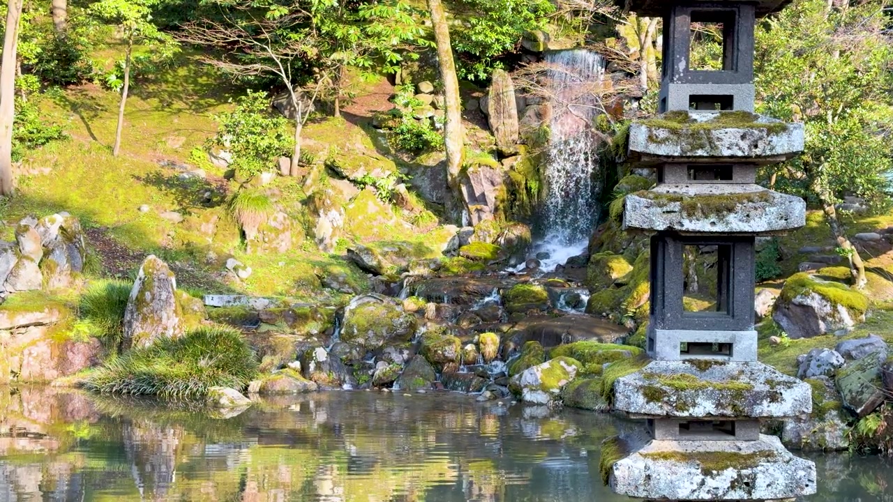 Inquadratura ampia statica di una lanterna di pagoda in pietra accanto a una cascata in un giardino giapponese