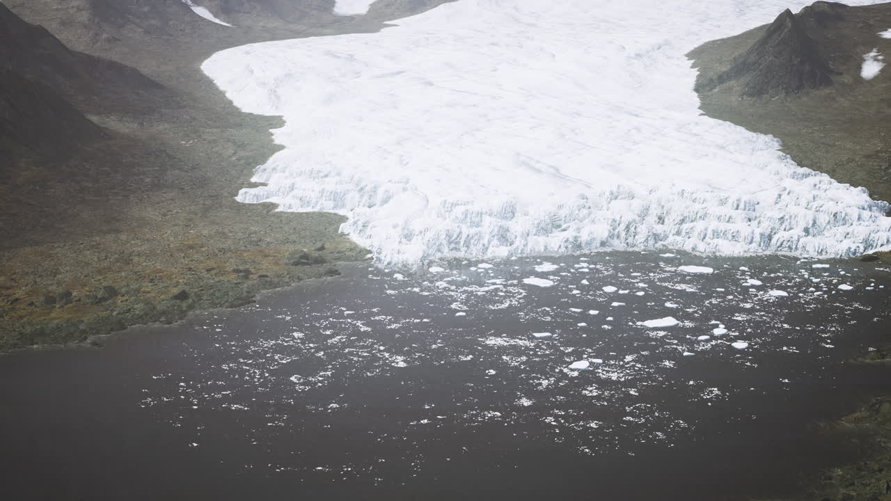 Glacier melting into water body near mountainous terrain under cloudy sky
