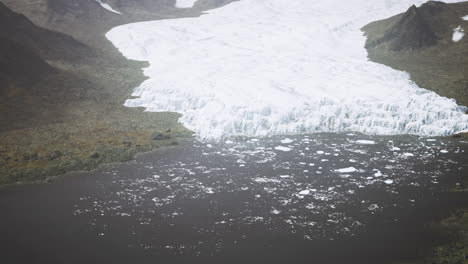 glacier melting into water body near mountainous terrain under cloudy sky