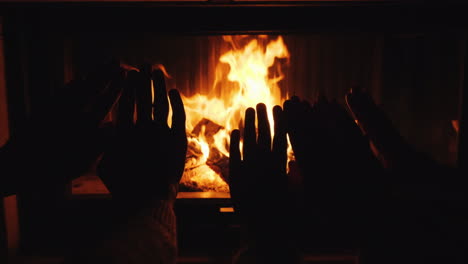 mom dad and baby warm their hands together by the fireplace