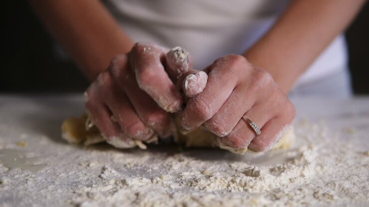 Close Up view of woman's hands kneading dough in flour on the table. Baker prepares the dough. Hands kneading dough. Slow