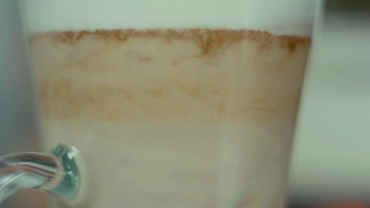 Coffee latte in glass layers mix up with spoon close up