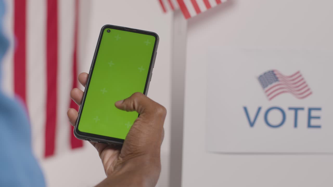 un hombre con un teléfono móvil de pantalla verde frente a una urna electoral en las elecciones estadounidenses