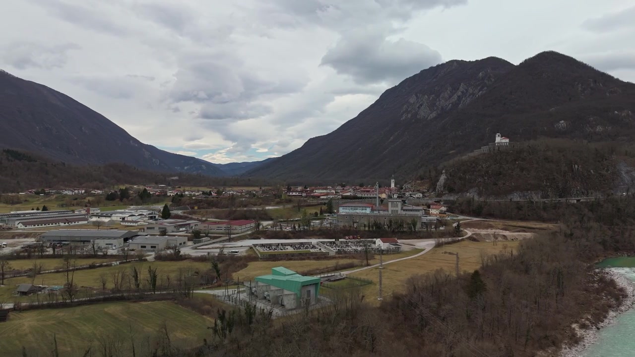 Kobarid nella Valle del Soča in Slovenia con il fiume Soča turchese, edifici del villaggio, chiesa, campi e montagne alpine in un paesaggio invernale, ripreso da una vista aerea.