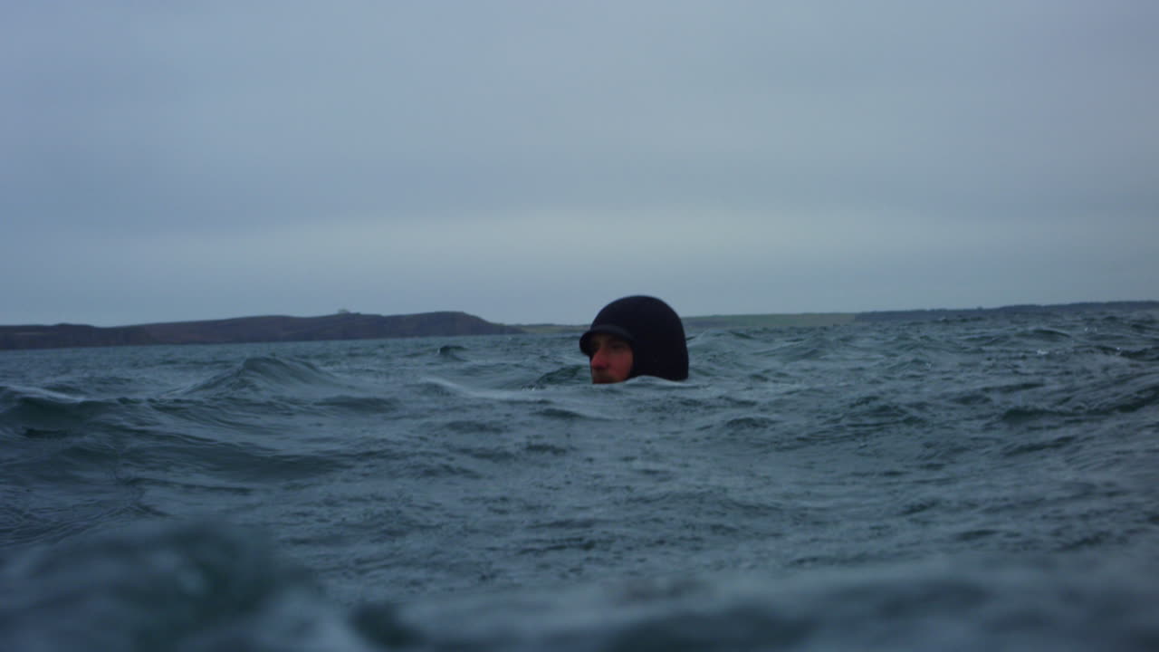 Photographer partially submerged scanning horizon while steadying camera in Atlantic swells, rocky churning surface