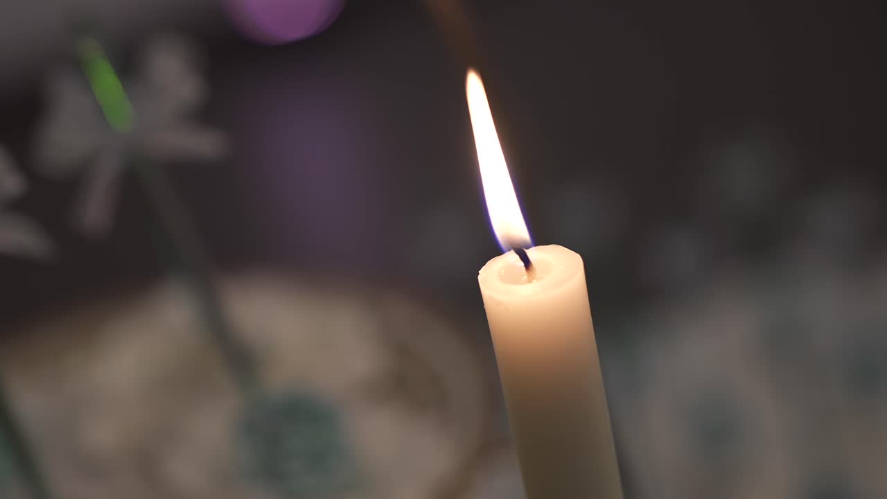 Close-up footage of single white candle flame burning with blurred party atmosphere in the background