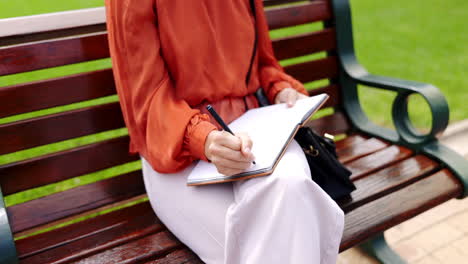 parque, banco y una mujer escribiendo en un cuaderno