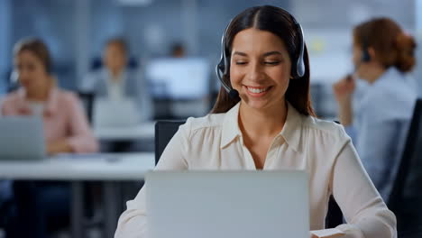 smiling woman with headset working on laptop in a call center