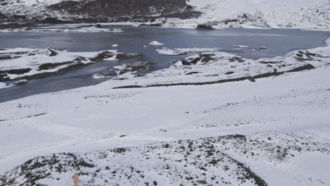 slow aerial revealing shot of a half-frozen lake at the base of icelandic mountains