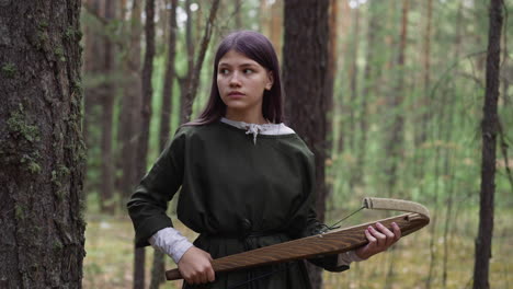 watchful girl holds crossbow hunting on animals in forest