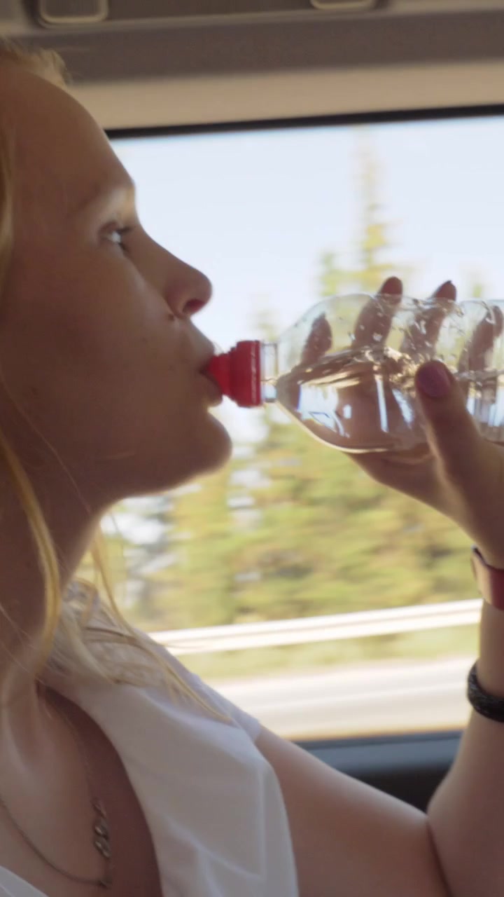 Mutter stillt Baby und trinkt Wasser im Auto.