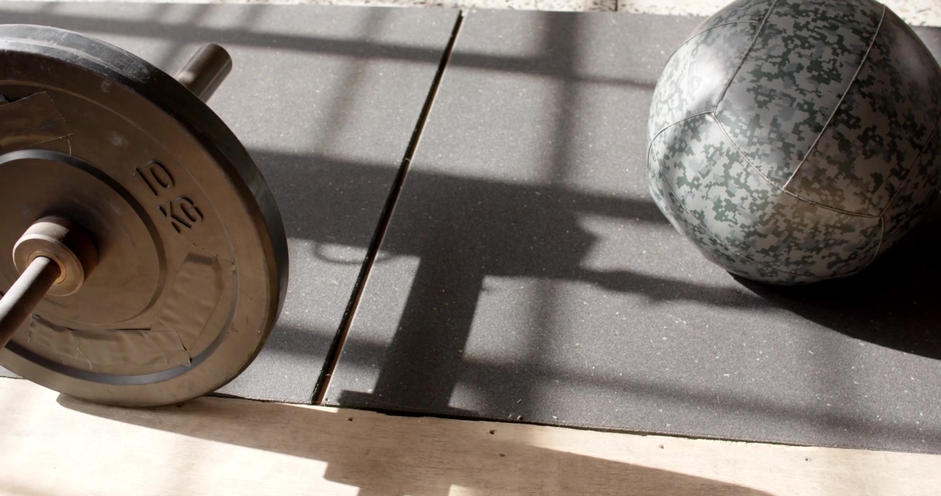 Camera is panning right up, revealing 10kg plate, medicine ball on mat near window showing training