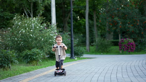 beautiful smiling baby riding his scooter approaching camera. lovely toddler having active time in the beautiful park in summer.