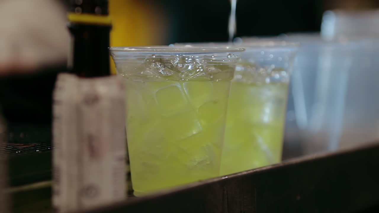 Bartender pours yellow mixer into iced cups in slow motion