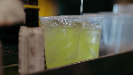 bartender pours yellow mixer into iced cups in slow motion