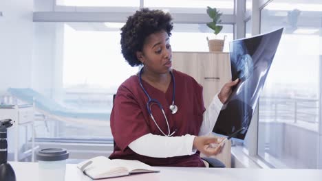 African-american-female-doctor-holding-x-ray-image-making-video-call-in-hospital-office,-slow-motion