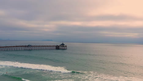 Drone-Vuela-Hacia-El-Muelle-De-La-Playa-Imperial-Sobre-Las-Olas-Del-Océano-Y-Los-Surfistas-En-San-Diego,-California---Toma-Aérea