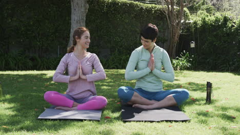 Feliz-Pareja-De-Lesbianas-Caucásicas-Practicando-Yoga-En-Un-Jardín-Soleado,-Cámara-Lenta