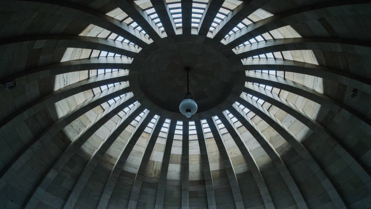 Luce solare che attraversa le finestre a cleristorio proiettando fasce sul soffitto a cupola, illuminando un globo pendente