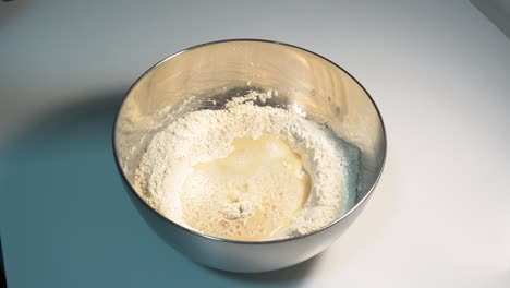 mixing ingredients in a stainless steel bowl on a white tabletop, pizza dough, bread dough