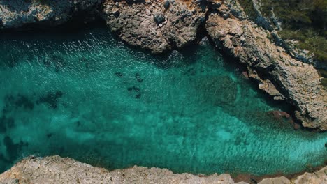 Clear-turquoise-blue-sea-water-in-a-remote-natural-bay-with-white-sand-beach,-Palma-de-Mallorca-Island