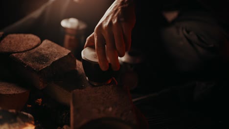 campfire coffee: young homeless guy sterilizes the water compartment of his old beat up moka pot in the flames of his campfire