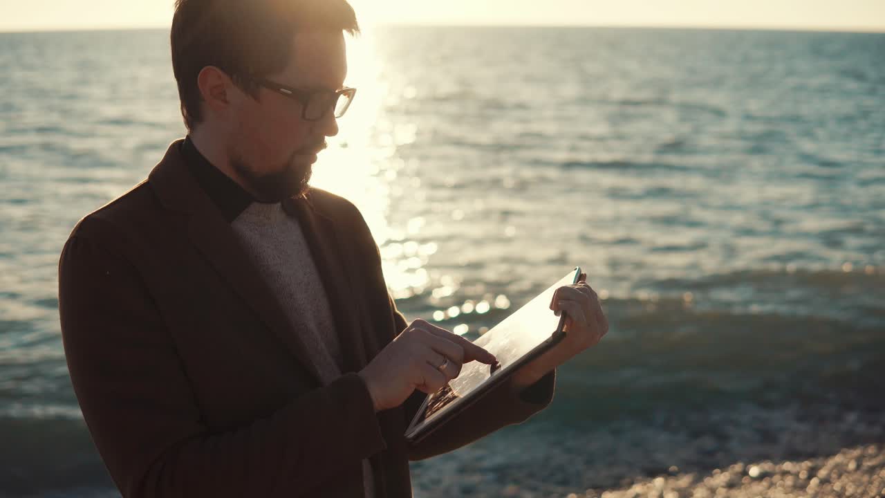 해가 지는 해변에서 태블릿을 사용하는 남자