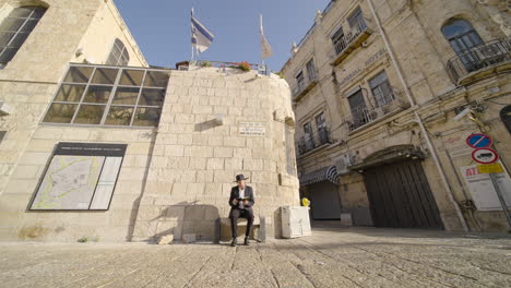 orthodox jewish man in his 30s praying on a stone bench in the historic old city of david, jerusalem, israel
