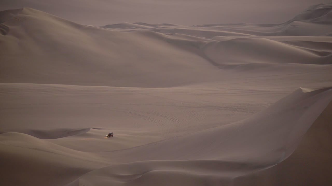 Peruvian desert landscape view with a quad speeding between dunes, at dusk