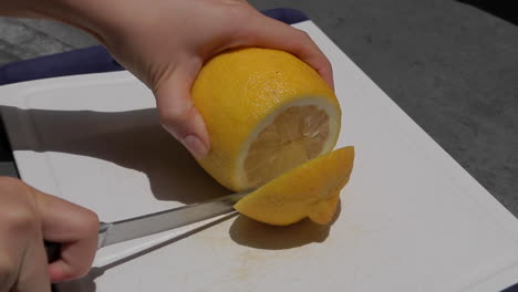 hand holding knife, cutting lemon on plastic board