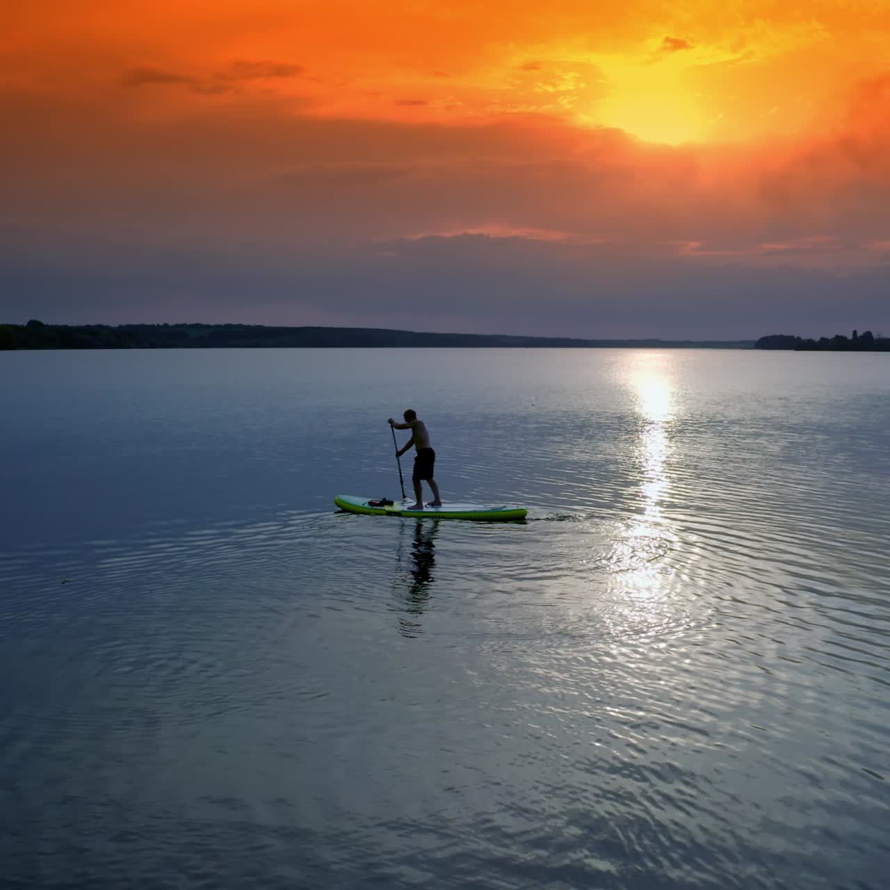 Man sailing on river. Sports training on water against beautiful sunset. Athlete is rowing on the evening water while standing with an oar. Water sports