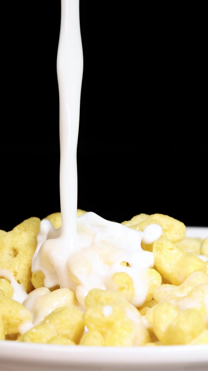 Il latte si riversa su cereali a forma di stella in una ciotola bianca su uno sfondo nero, creando una dinamica scena per la colazione