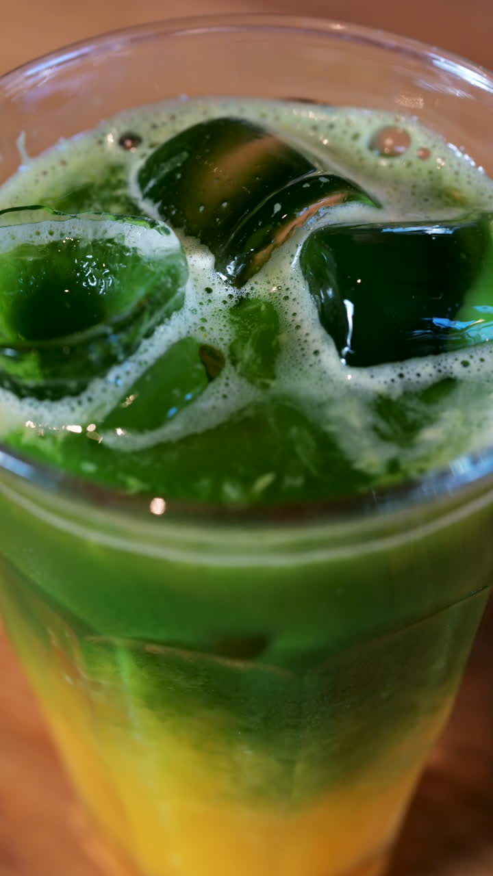 Close up of a glass of an iced orange juice matcha on a table at a cafe. Vertical