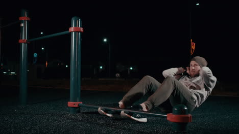 hombre haciendo abdominales en una estación de entrenamiento en la calle por la noche