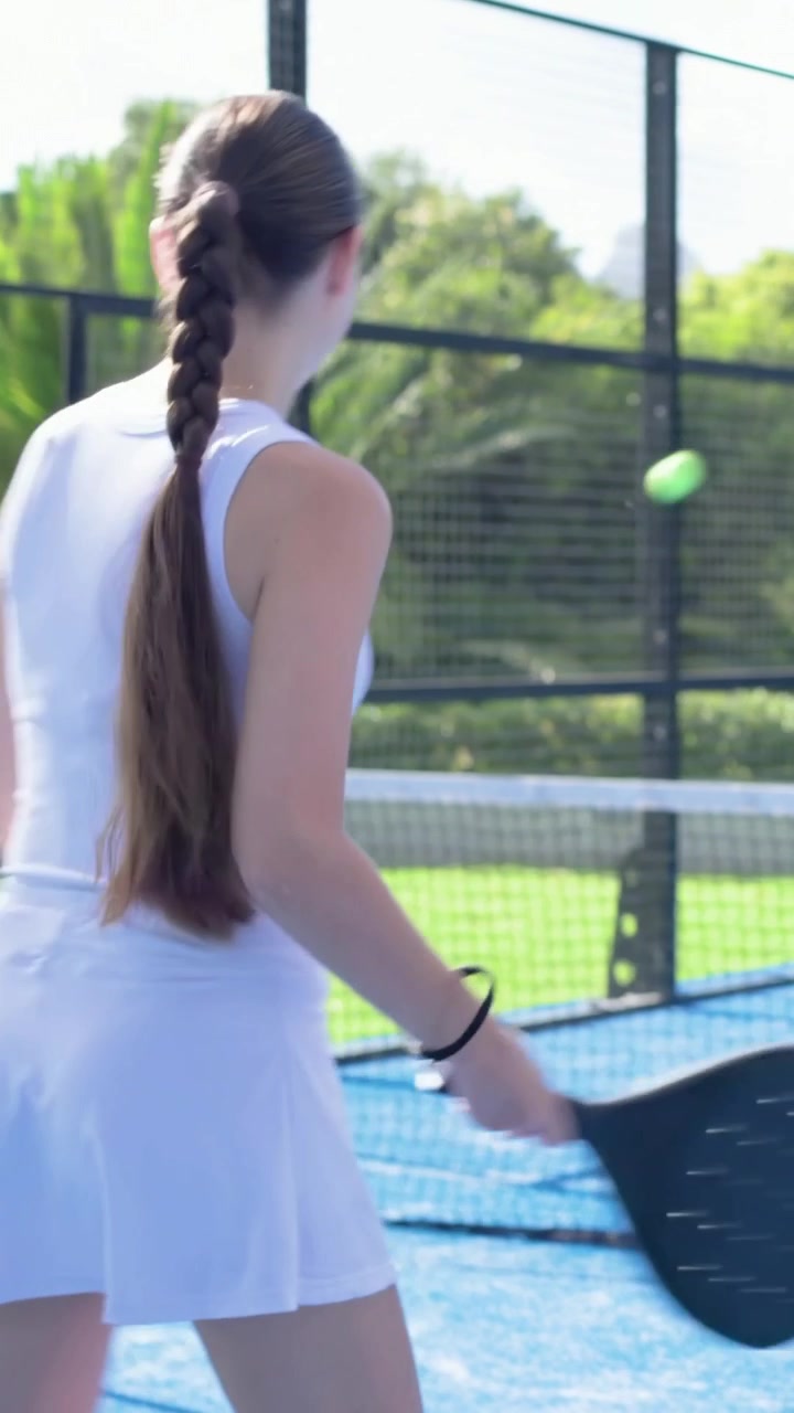 Vertical video: Preparing woman in white returning ball near net with padel racket on blue court