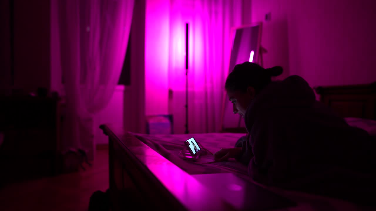 mujer usando el teléfono en el dormitorio por la noche con luz rosa