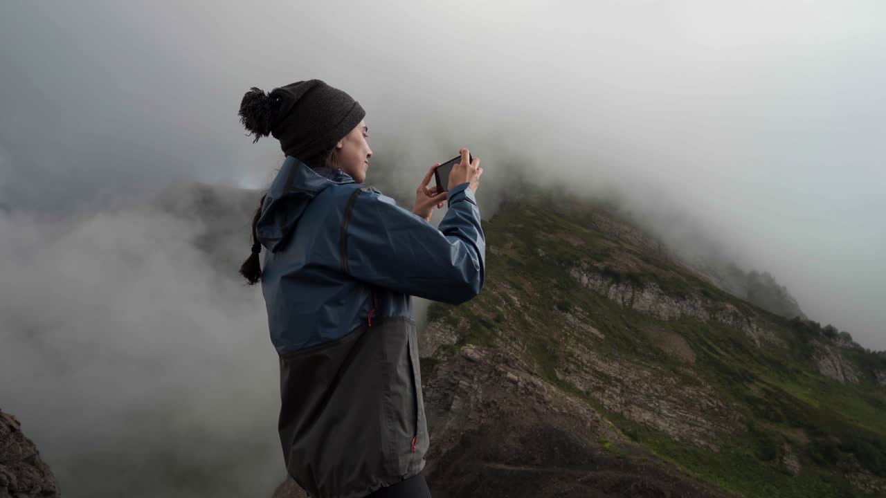 Young Woman Taking Photo of Misty Mountain Landscape with Smartphone