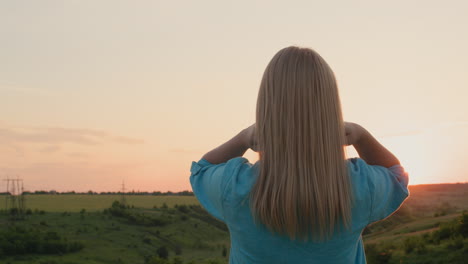 a woman straightens her hair, stands against the backdrop of a picturesque landscape where the sun sets