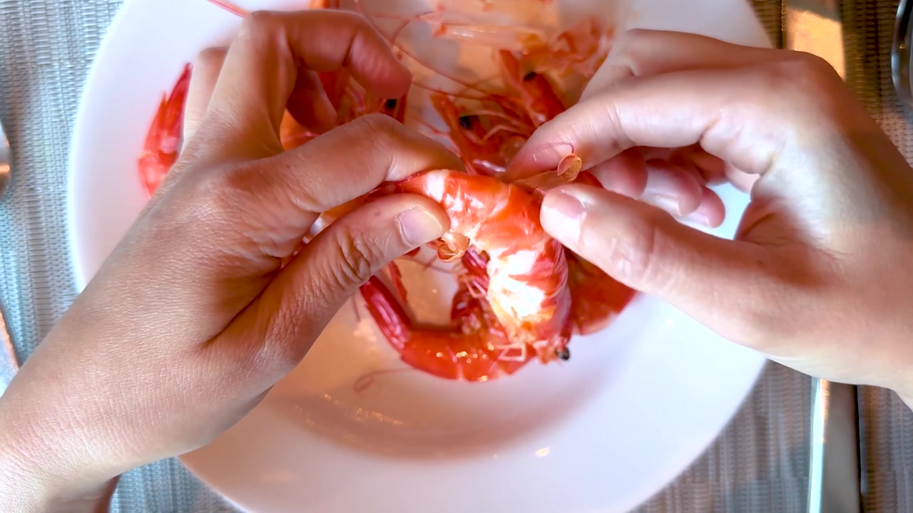 Overhead shot of hands peeling fresh cooked shrimp on a white plate in a restaurant