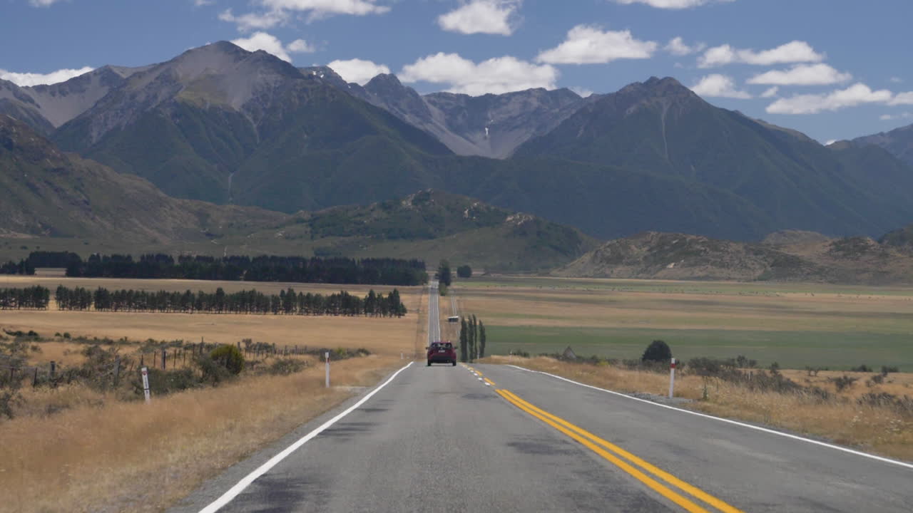 fotografia em câmera lenta de um carro a descer uma estrada em direção às montanhas - arthur's pass, nova zelândia