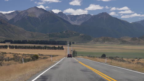 slow motion shot of a car driving down a road towards mountains - arthur's pass, new zealand