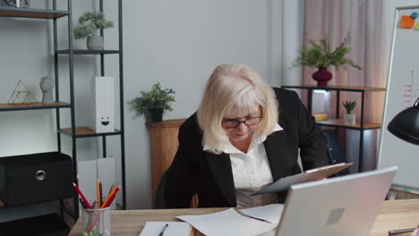 senior business woman examining graphs, analyzing, managing finance documents report at home office