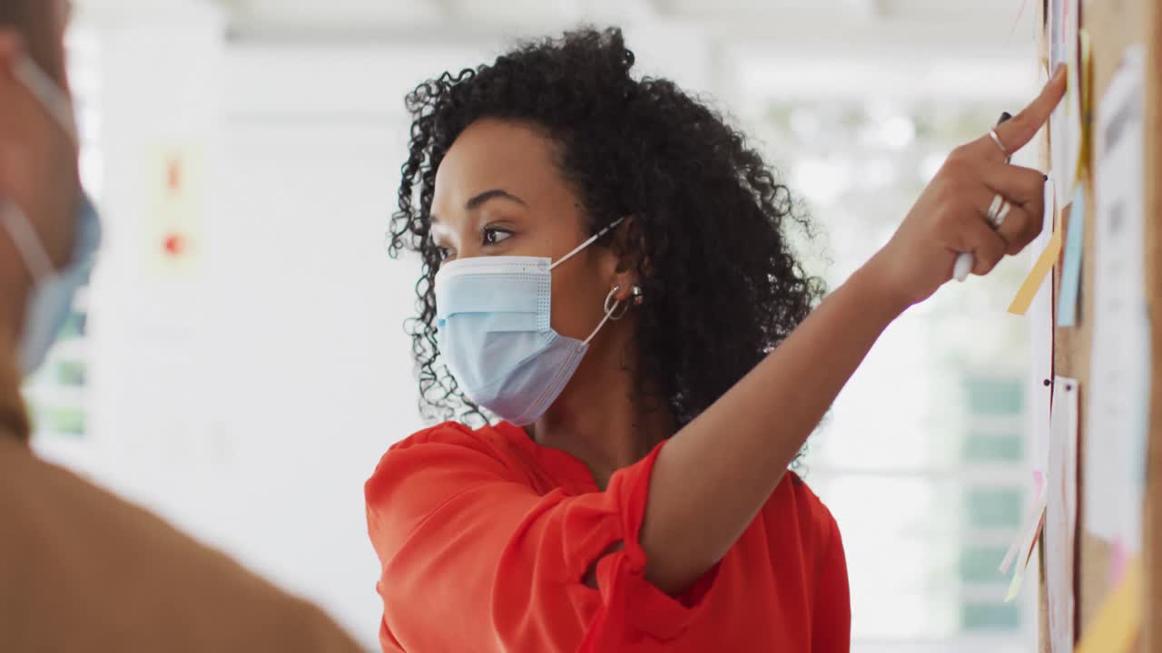 Woman wearing face mask discussing over memo notes with her colleagues at office