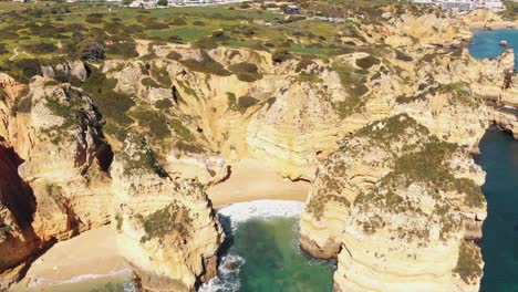 secluded pinheiros beach surrounded by jagged rock formations in lagos, algarve, portugal - aerial fly-back tilt-up shot