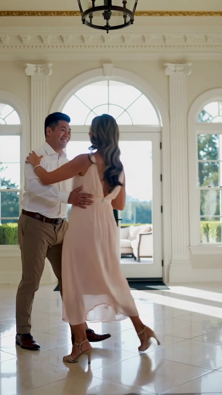 Vertical video: Reaching man in white shirt guiding woman in pink dress into dance in foyer