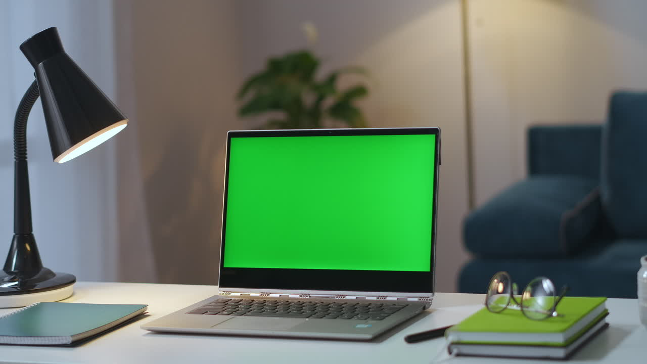 tavolo di lavoro in ufficio a casa di freelance o lavoratore remoto portatile con chroma key display lampada occhiali e libri colpo statico in appartamento